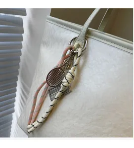 Detail of silver tennis racket and abacus charms on a textured cream tote bag