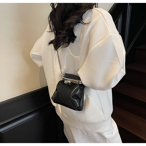 Detail shot of black patent leather mini bucket bag with silver metal chain and clasp