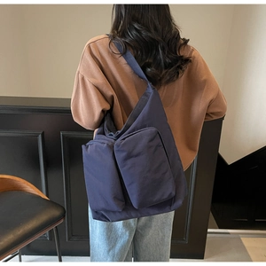 Detail of dark blue canvas tote bag with dual front pockets shown on model shoulder