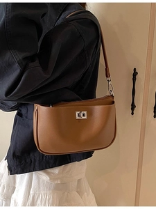 Chic brown leather underarm bag with silver lock worn by a model in casual attire