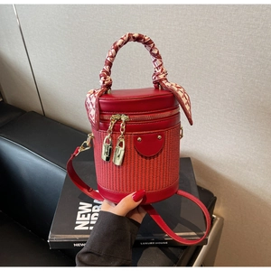 Detail of red cylindrical bucket bag featuring woven texture and silk scarf handle