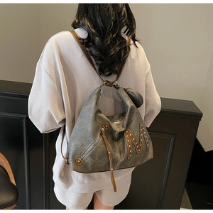 Close-up of distressed grey hobo bag featuring rivet studs and long brown leather tassels
