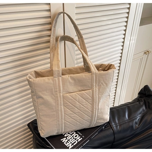 Close-up of beige quilted tote bag showing the front pocket and padded puffer texture