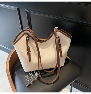 Detail of cream suede tote bag with brown leather trim and WWTU logo on a leather chair