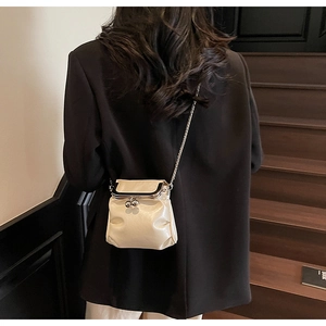 Model wearing a cream chain crossbody bag with pleated texture and silver metal clasp