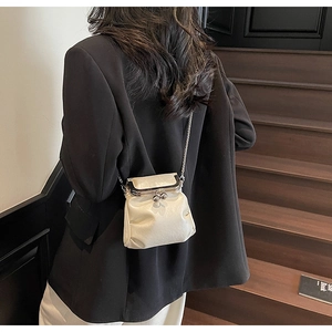 Detail of cream pleated mini crossbody bag with silver clasp and metal chain strap