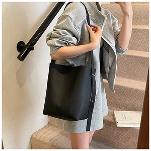 Detailed view of black litchi pattern bucket bag with embossed logo on street style model