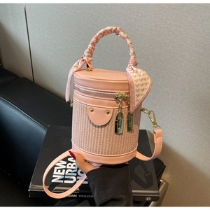 Detail view of pink cylinder bag with woven texture, silk-wrapped handle and gold hardware
