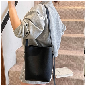 Detail of black pebbled leather bucket bag with embossed logo and slim shoulder strap