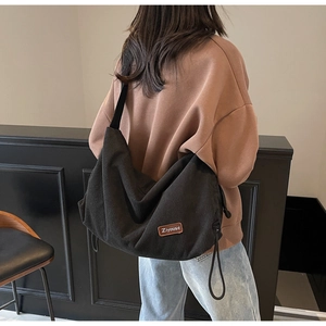 Detail of black corduroy messenger bag featuring side drawstring and brand patch