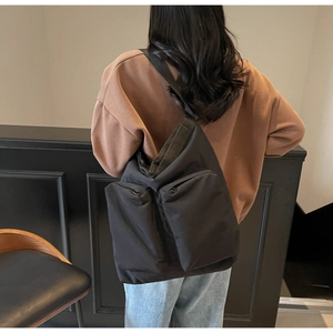 Rear view of a model wearing a large black nylon shoulder bag with two large front pockets