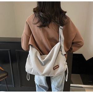 Detail shot of light blue corduroy crossbody bag with brown leather label and drawstring