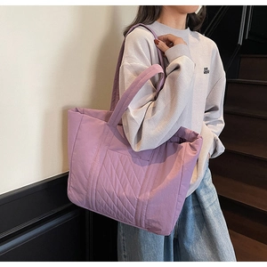 Close-up of a purple quilted tote bag with wide shoulder straps worn in an indoor setting