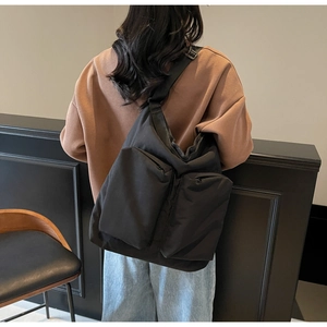 Detail of a black puffy nylon crossbody bag with dual front pockets and wide strap