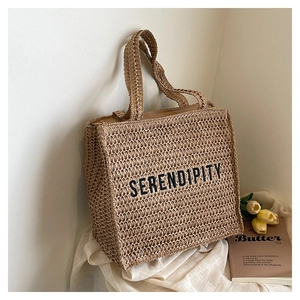 Detail view of the black SERENDIPITY embroidery on this beige woven beach tote bag