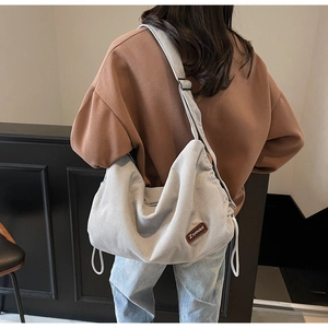 Detail of light gray corduroy hobo bag with drawstring side and brown leather logo tag