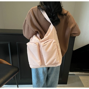 Detail of light pink shoulder bag featuring dual front zipper pockets and wide strap