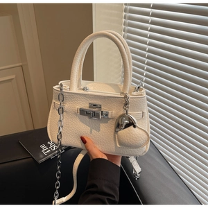 Detail of white lychee leather bucket bag with silver clasp and heart charm on a sofa