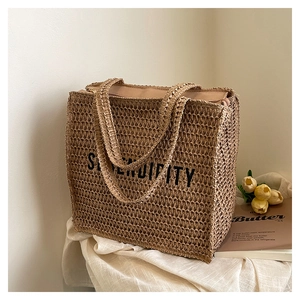 Detail view of woven straw tote bag with black SERENDIPITY text and zipper closure