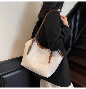 Detail of the large beige tote bag with brown straps and buckle accents worn by a model