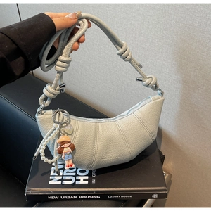 Detail of light blue crescent bag featuring knotted strap and decorative charms with pearls
