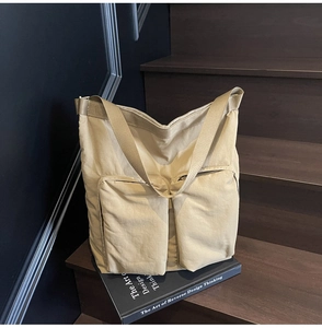 Close-up of khaki nylon tote bag with two front zipper pockets on dark wooden stairs