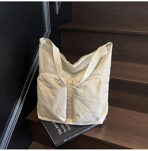 Detail of off-white tote bag showing dual front pockets and wide strap on wooden steps
