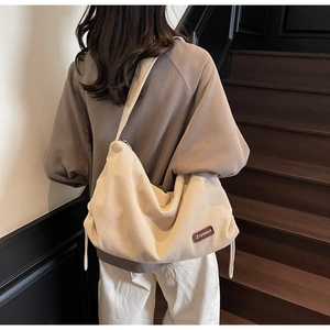 Close-up of cream corduroy crossbody bag texture and logo detail on a wooden staircase