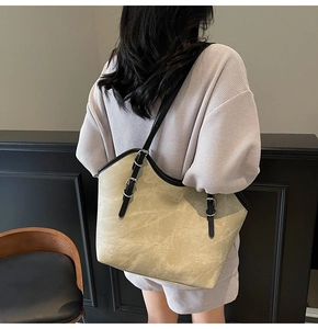Detail of beige tote bag showing black piping and silver buckles on the strap