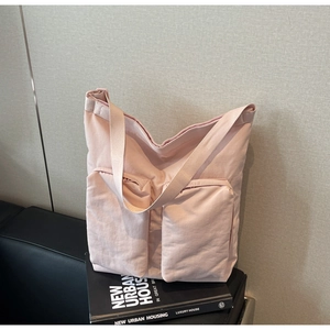 Detail of a pink nylon tote bag with double front zipper pockets on a black leather sofa