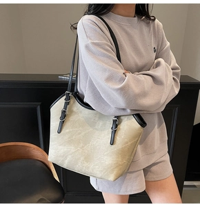 Detail of large beige tote bag featuring black contrast trim and adjustable buckle strap