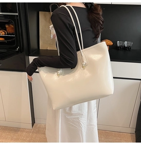 Close-up of a high-gloss off-white tote bag featuring elegant knotted shoulder strap details