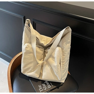 Detail view of large cream canvas tote bag with front zipper pockets on a black chair