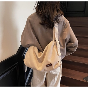 Detail of cream corduroy crossbody bag featuring a leather logo patch and drawstring sides