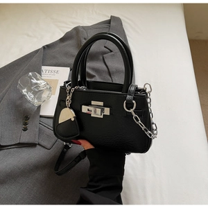 Detail of black textured bucket bag with silver metal twist lock and heart pendant charm