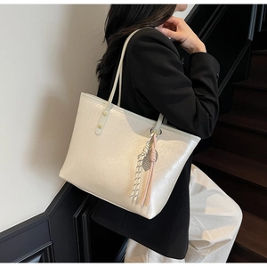 Detail view of cream-white tote bag with textured faux leather and elegant tassel charm