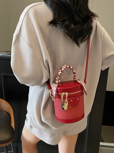 Red cylindrical barrel bag with woven texture and silk scarf wrapped handle on shoulder