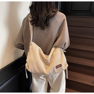 Detail of beige corduroy shoulder bag with brown leather logo patch on wooden stairs