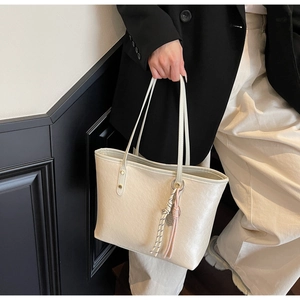 Detail of a beige tote bag featuring a trendy woven rope tassel and slim shoulder strap
