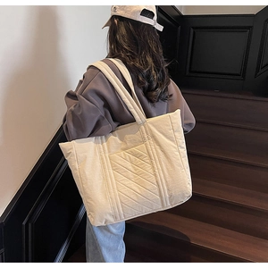 Quilted beige canvas tote bag with diamond stitching shown in use on a shoulder