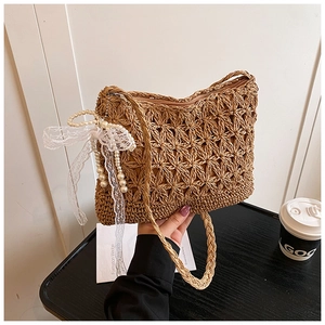 Detail der handgewebten Strohtasche mit Spitzenschleife, Perlenanhänger und Häkeltextur