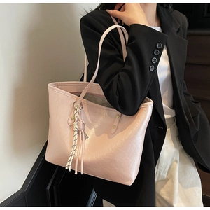 Close-up of pink faux leather tote bag with braided tassel detail and long shoulder straps