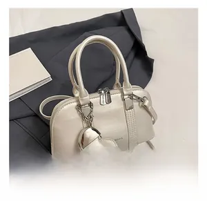 Detailed view of cream shell bag with heart charm and zipper on grey blazer background