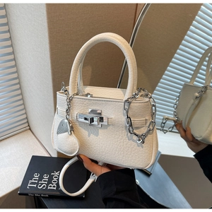 Detailed view of white bucket bag with silver twist lock and heart charm accessory