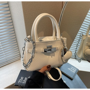Detail of cream bucket bag showing lychee leather texture, silver chain, and heart charm