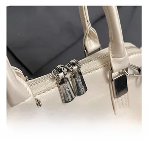 Macro shot of silver dual zippers and fine leather texture on a cream shell bag