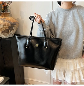 Detailed view of black glossy tote bag with gold logo and slim handles on model