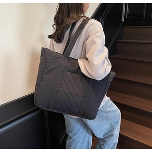 Rear view of model carrying a large black quilted tote bag on wooden stairs