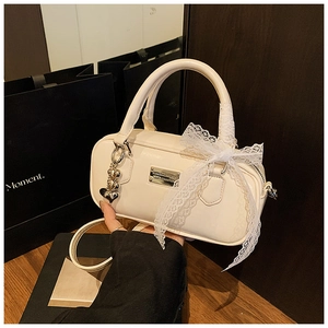 Detail of cream bowling bag featuring lace bow, silver heart charm and PU leather texture