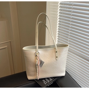 Detailed side view of cream tote bag featuring textured leather and woven tassel charm